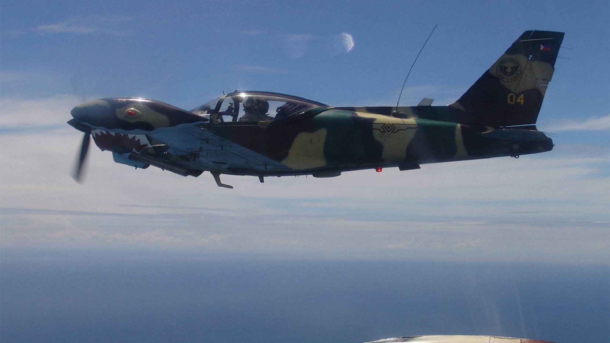 Een SF-260 van de Philippine Air Force in camouflagekleuren vliegt boven zee, met zicht op de cockpit en de draaiende propeller