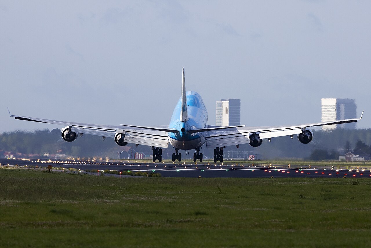 Een Boeing 747 van KLM landt op Schiphol met de romp schuin op de baan tegen de wind in, met de baanverlichting op de achtergrond