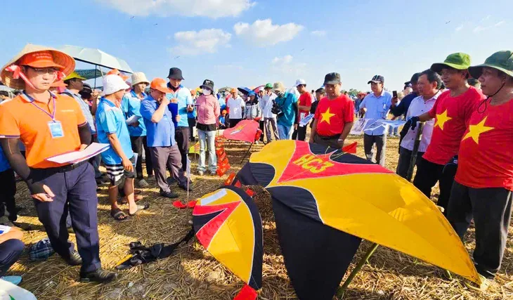 Grote geel-zwart-rode Vietnamese vliegers liggen op een stoppelveld tussen een groep mensen